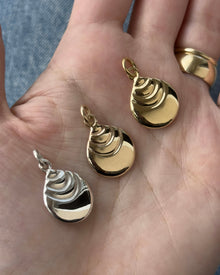 Three small hoju-shaped pendant charms are displayed on an open hand. Two are polished gold and one is silver.